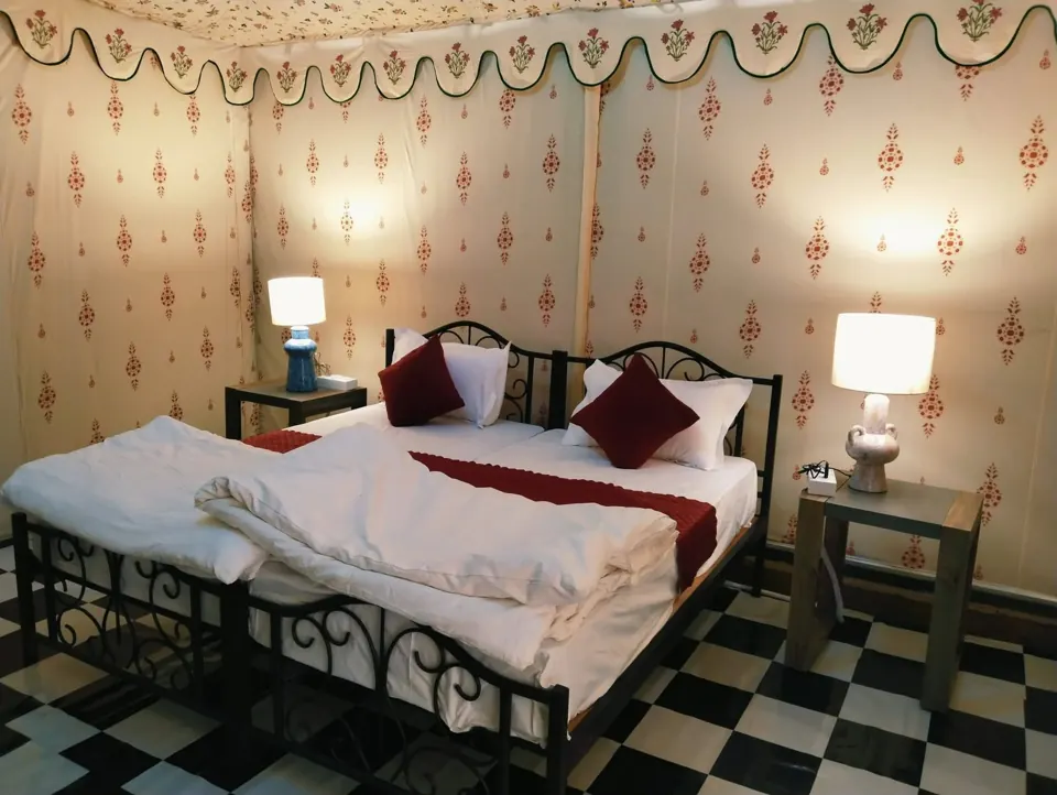 Furnished tent bedroom with white bedding, maroon cushions and bedside lamps